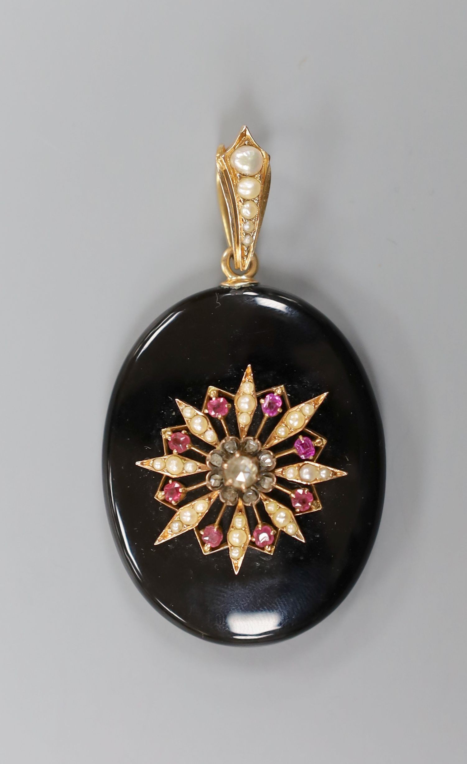 A Victorian black enamel, rose cut diamond, ruby coloured paste and seed pearl set oval mourning pendant, with glazed back and seed pearl set yellow metal bale, overall 69mm.